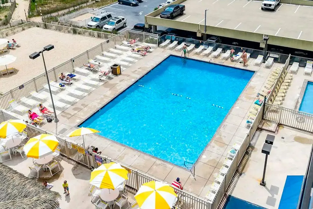 An outdoor swimming pool is surrounded by lounge chairs and yellow-and-white umbrellas.