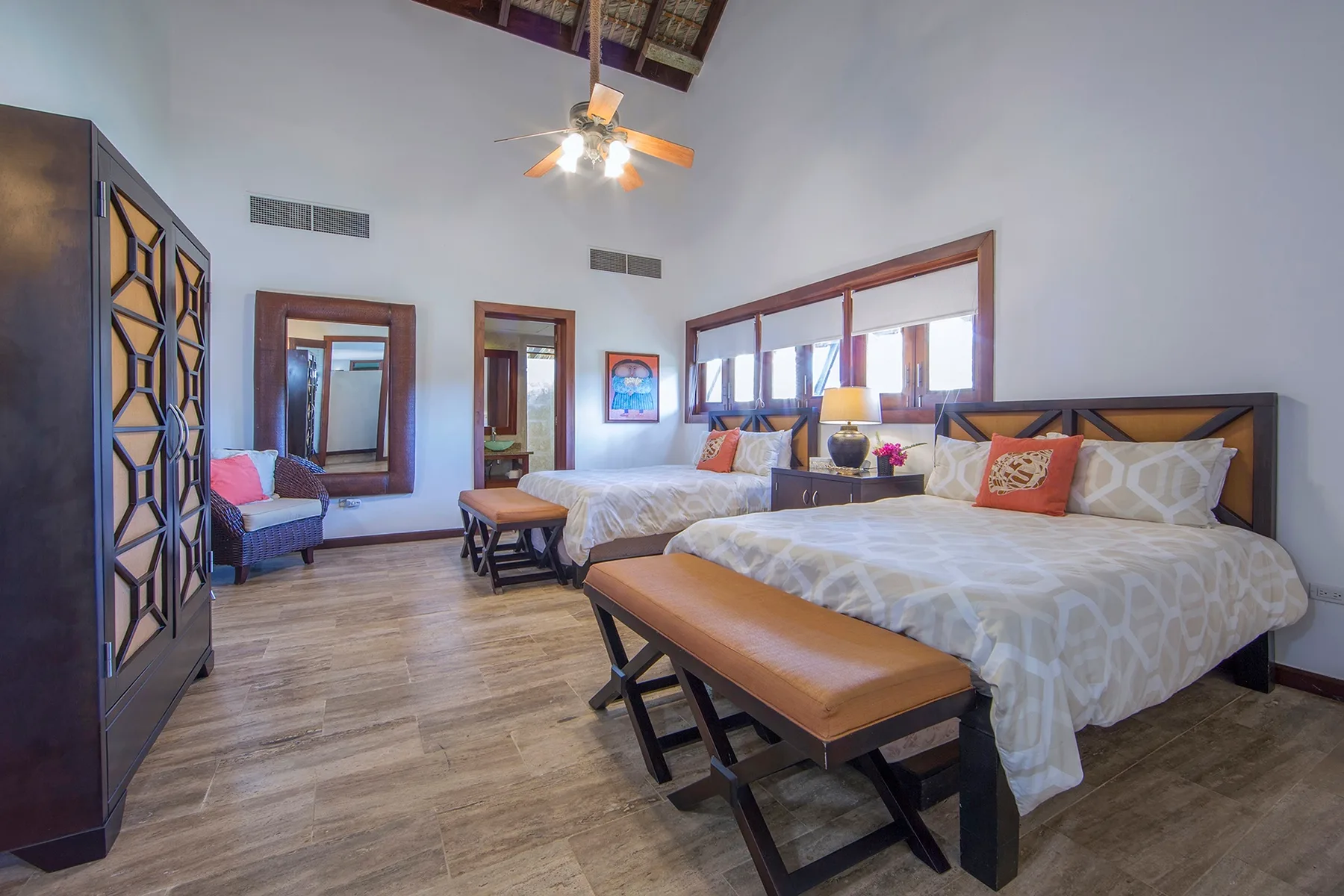 A bright bedroom with two beds and a wooden bench at the foot of one bed.