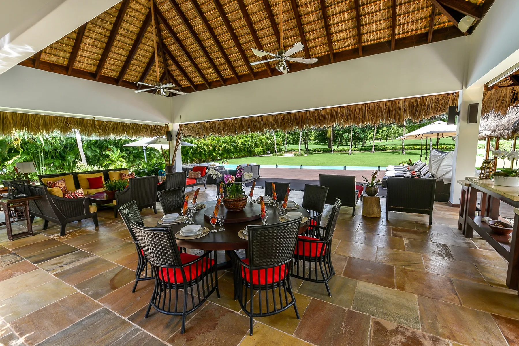 A covered outdoor dining area with tables, seating, and a garden view.