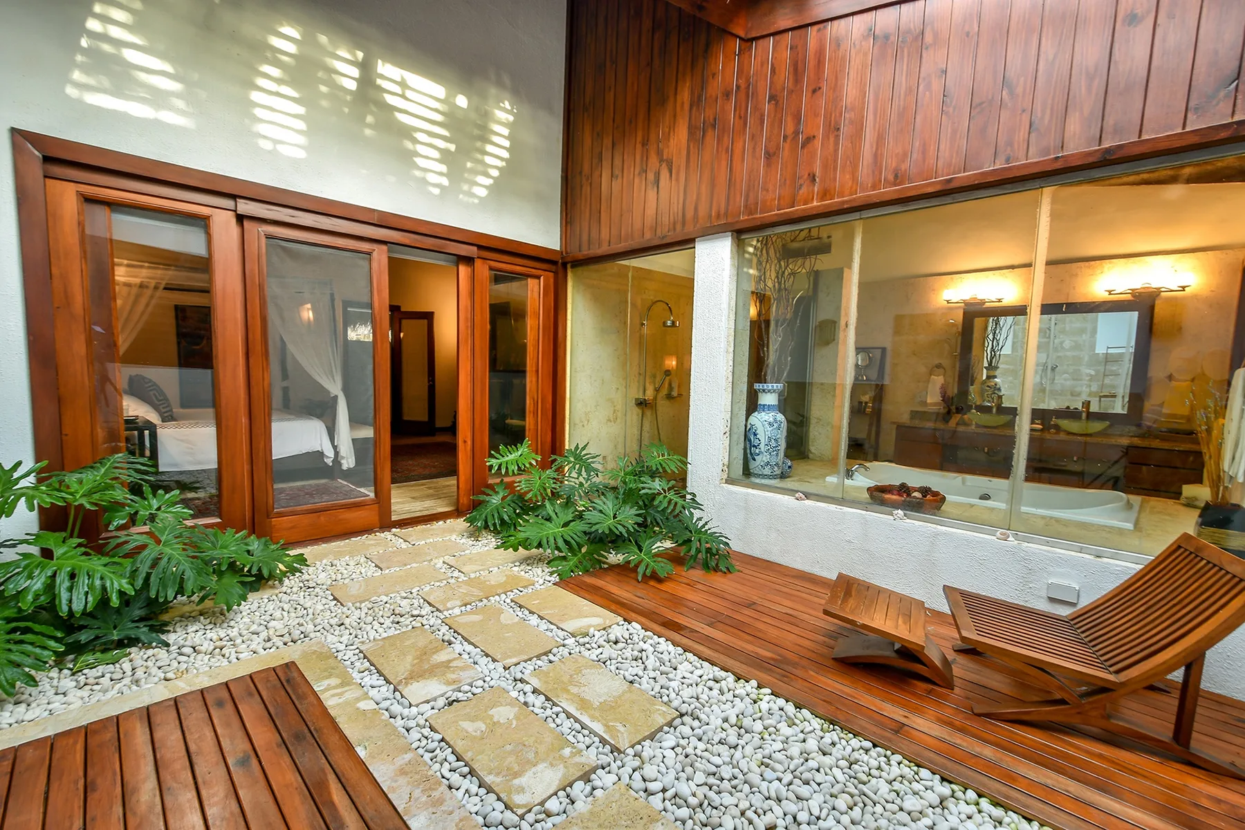 A wood-decked patio with lounge seating and a glass wall overlooking an interior room.