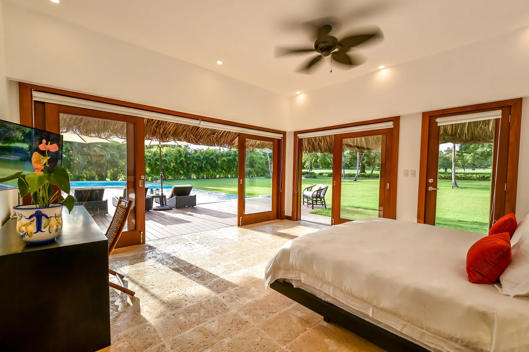 A bright bedroom opens onto a garden through several glass doors.