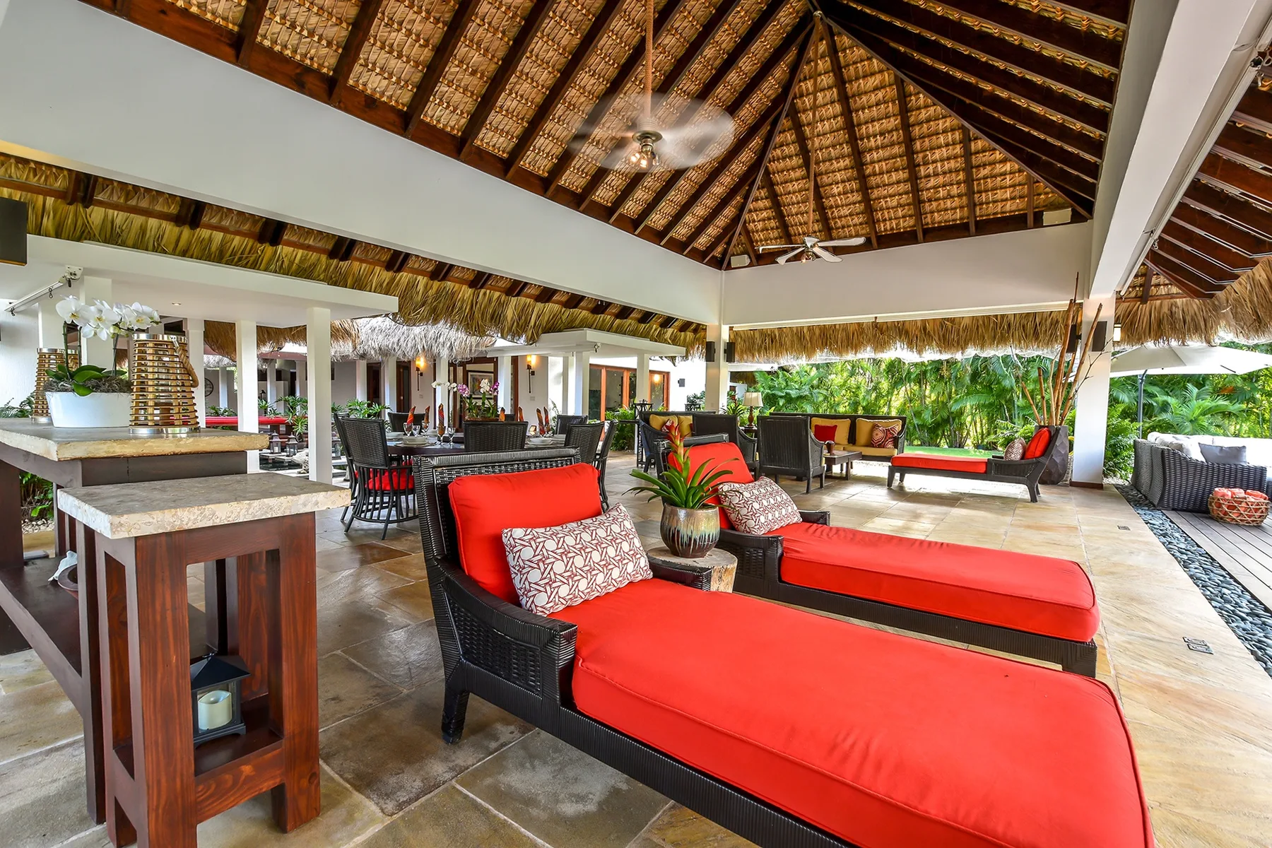 An open-air lounge with red cushioned seating beneath a thatched roof.