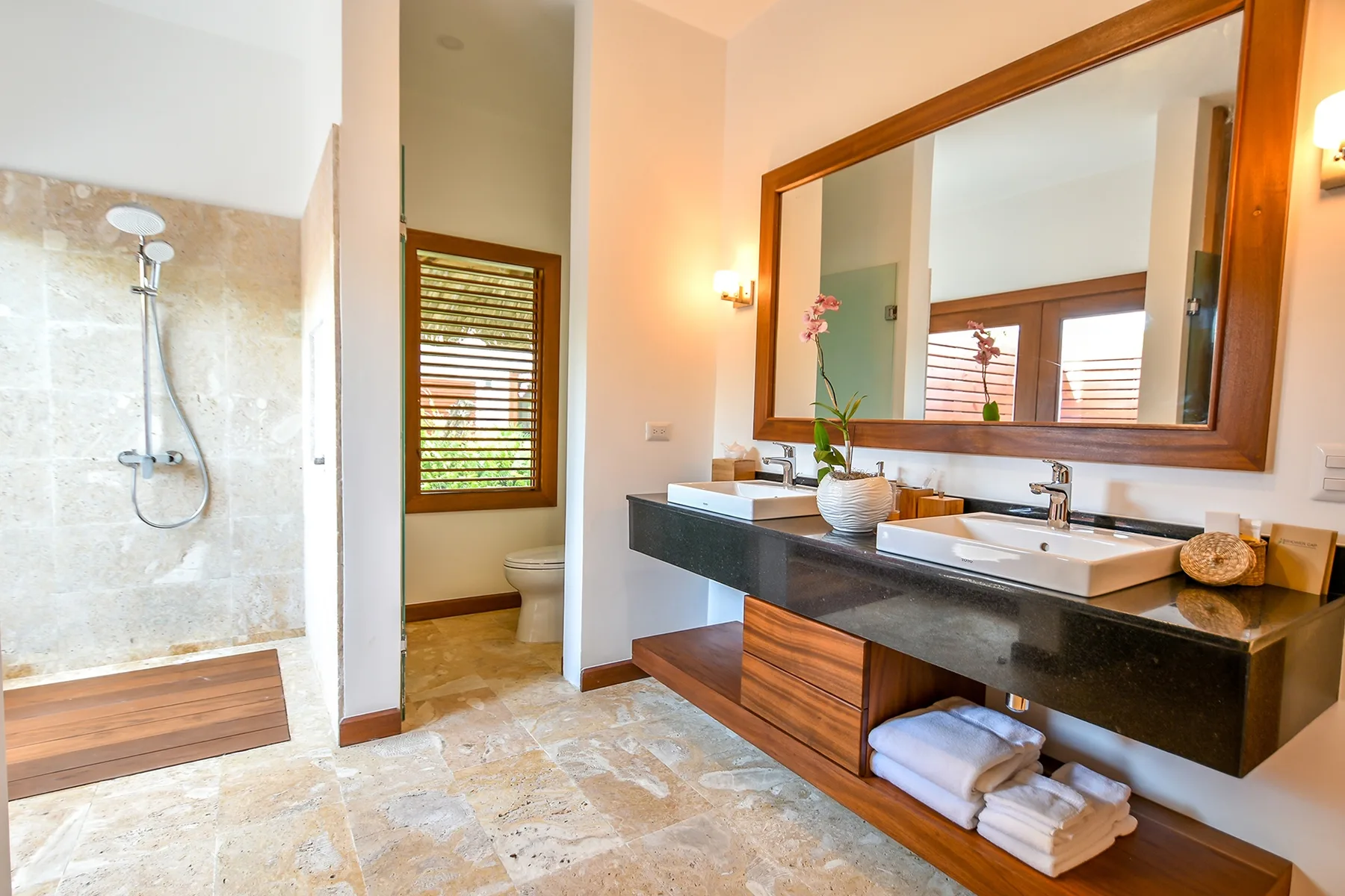 A bright bathroom with a walk-in shower and a long vanity beneath a large mirror.