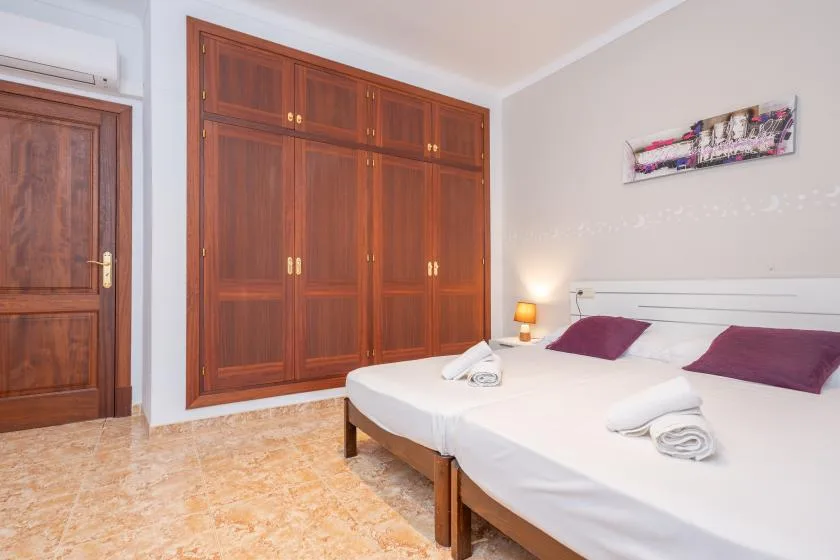 A bedroom with two beds, wooden wardrobes, and a wall-mounted air conditioner.