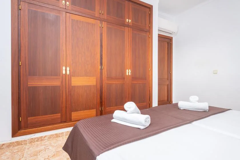 A bedroom with a bed in the foreground and a large wooden wardrobe.