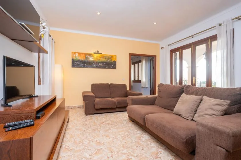 A living room with brown seating, a television, and large windows.