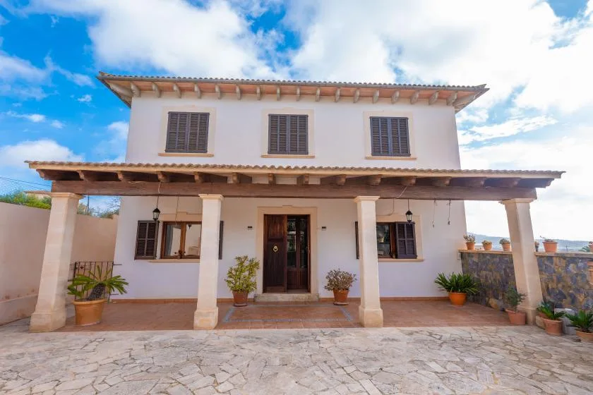 A two-story house with a covered porch and a stone-paved courtyard.