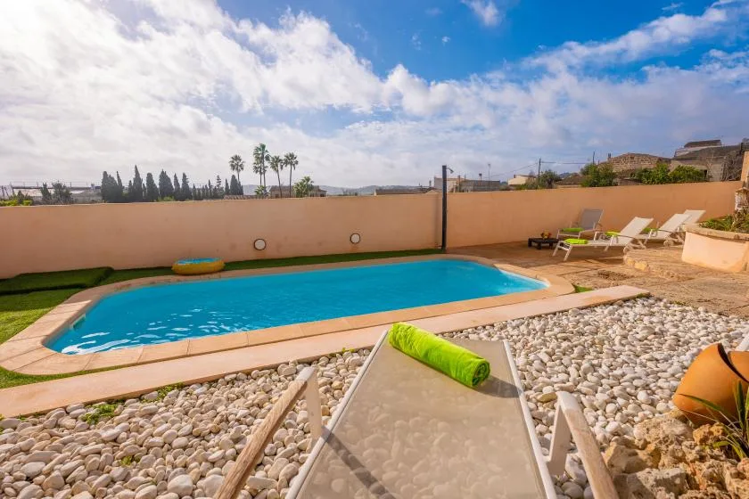 An outdoor swimming pool beside a stone-covered patio and lounge seating.