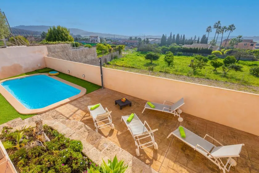 A sunny patio with a small swimming pool and lounge seating overlooks greenery.
