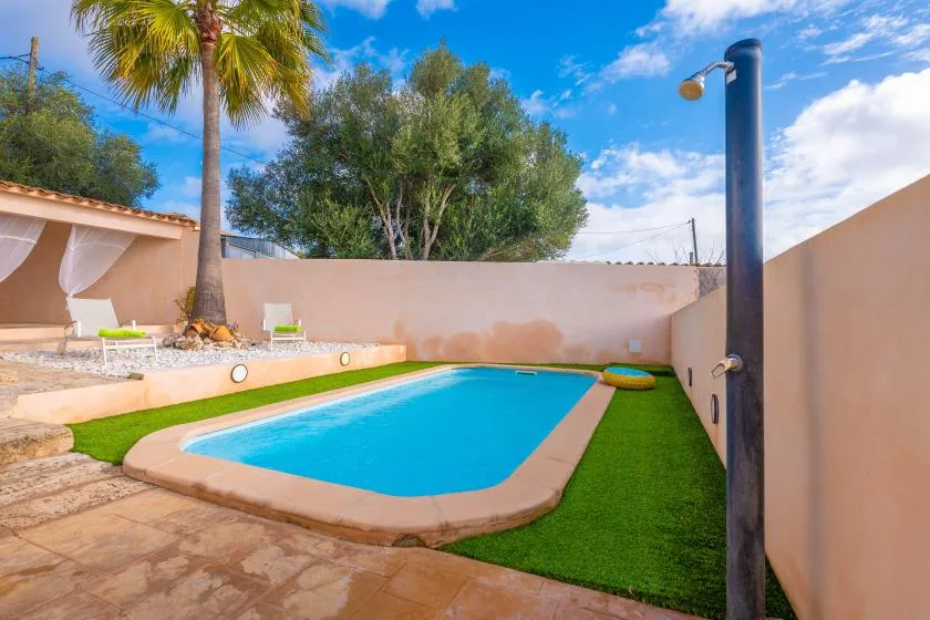 An outdoor swimming pool sits beside green turf in a walled patio.