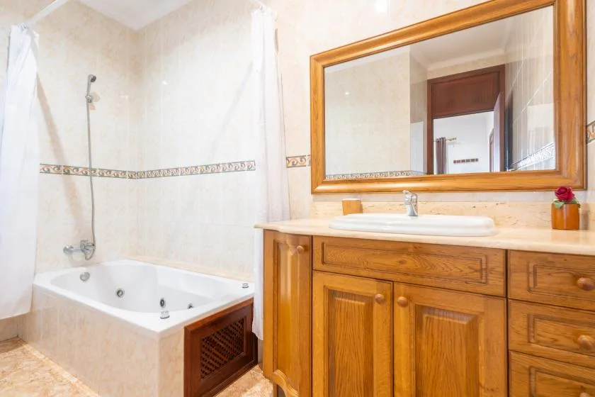 A bathroom with a bathtub, sink, and wooden vanity beneath a large mirror.