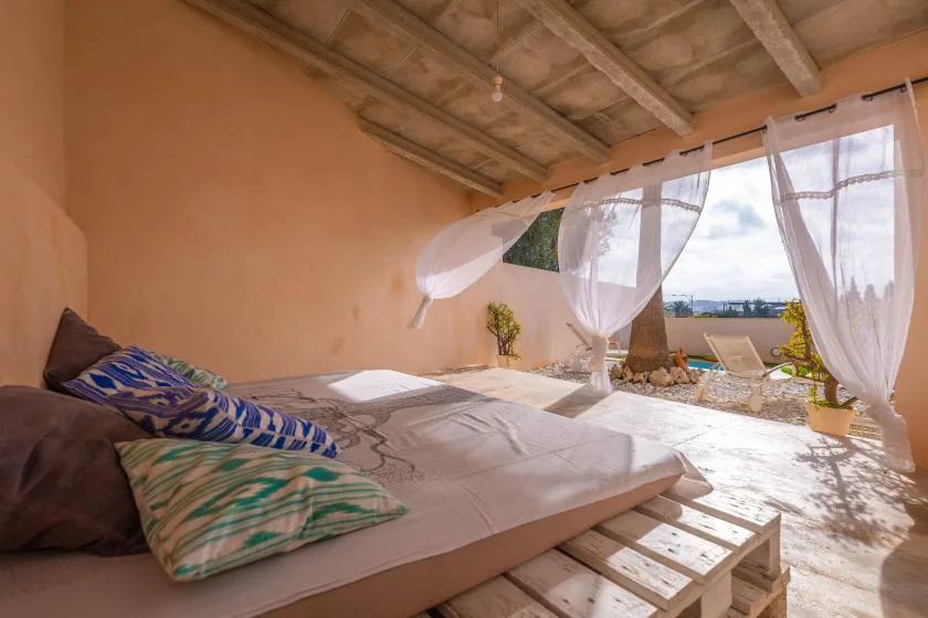 A bedroom with a low bed beside open curtains and a bright outdoor view.