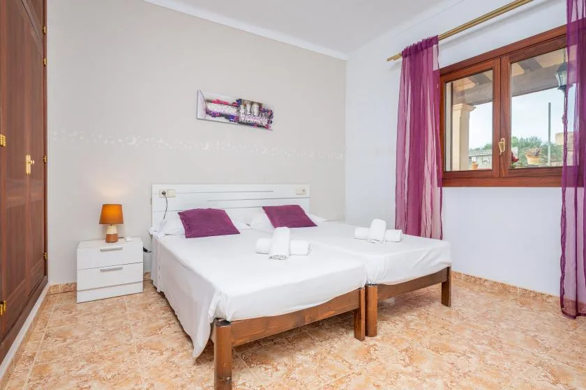 A bedroom with two beds, white bedding, and a window with purple curtains.