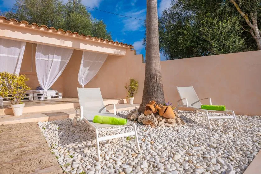 An outdoor patio with white lounge seating, pebble ground, and a shaded seating area.