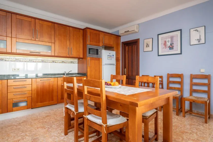 A dining area with a wooden table and chairs beside a fitted kitchen.