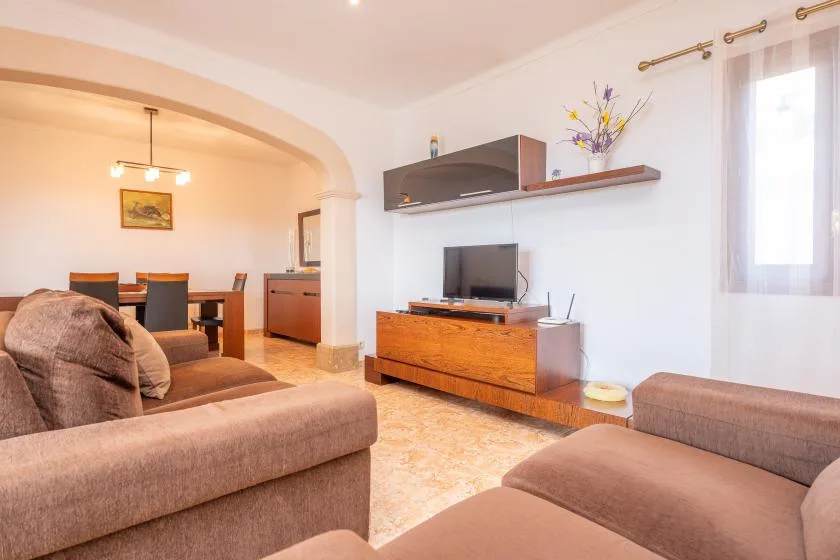 A living room with seating, a television, and a dining area beyond the archway.