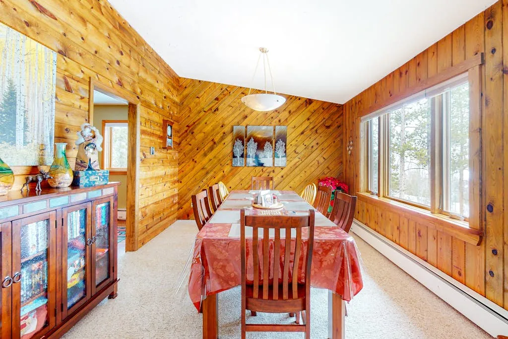 A wood-paneled dining room with a long table beside large windows.