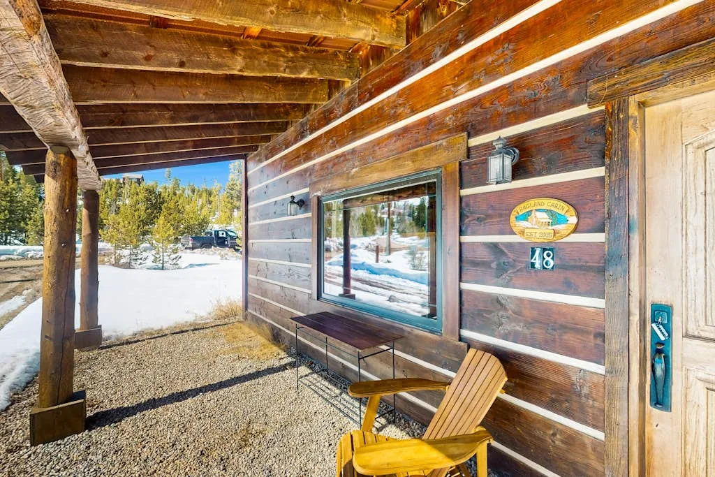 A covered wooden porch with a window and seating overlooks a snowy landscape.