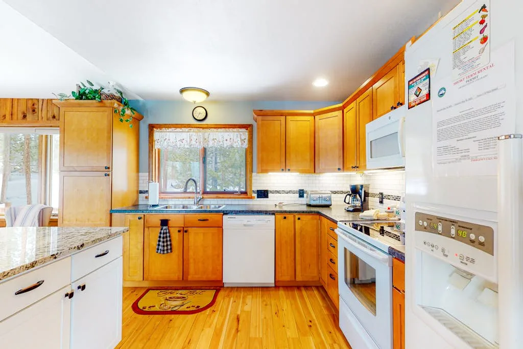 A bright kitchen with wooden cabinets, a central window, and kitchen appliances.