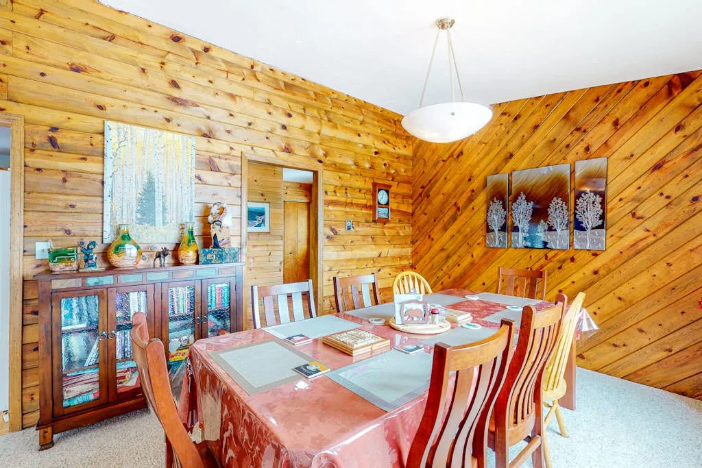 Comedor con una mesa larga, asientos de madera y paredes revestidas de madera.