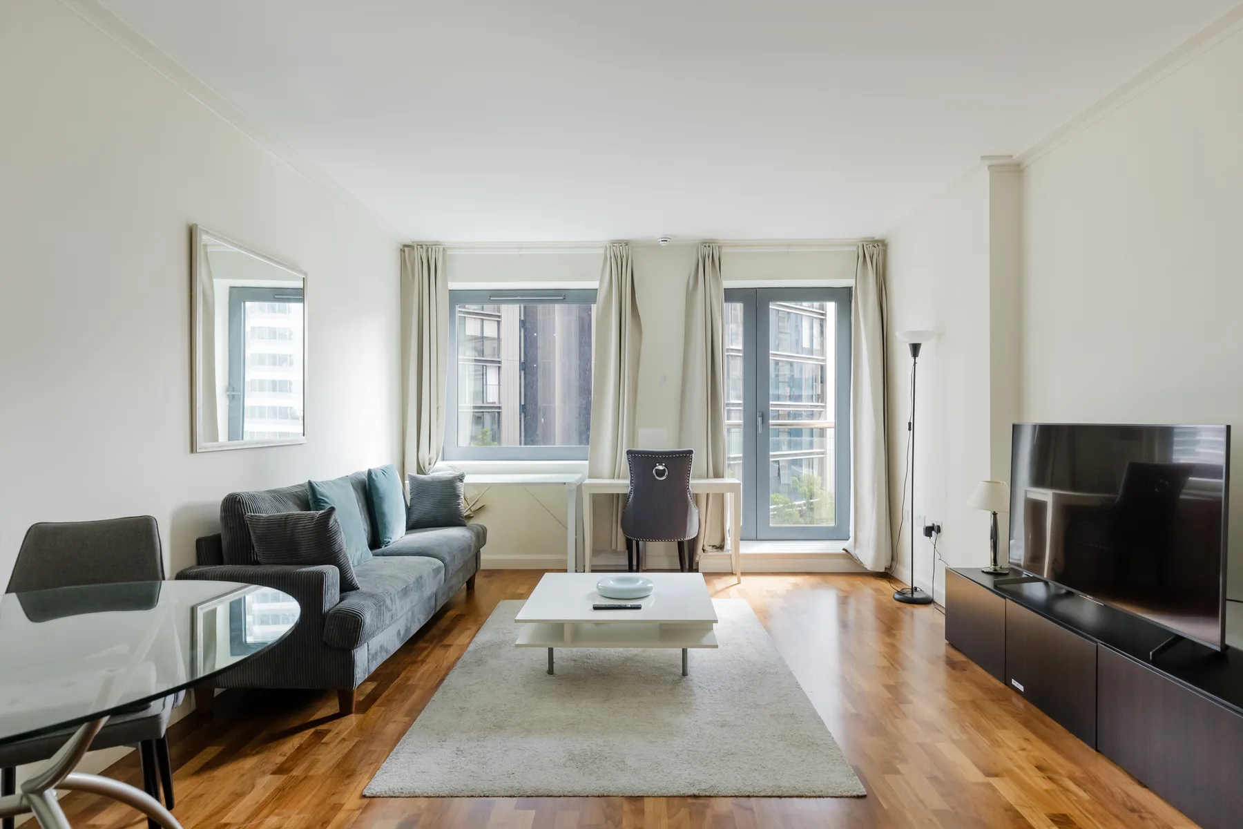 Living room with seating, a coffee table, and windows overlooking nearby buildings.