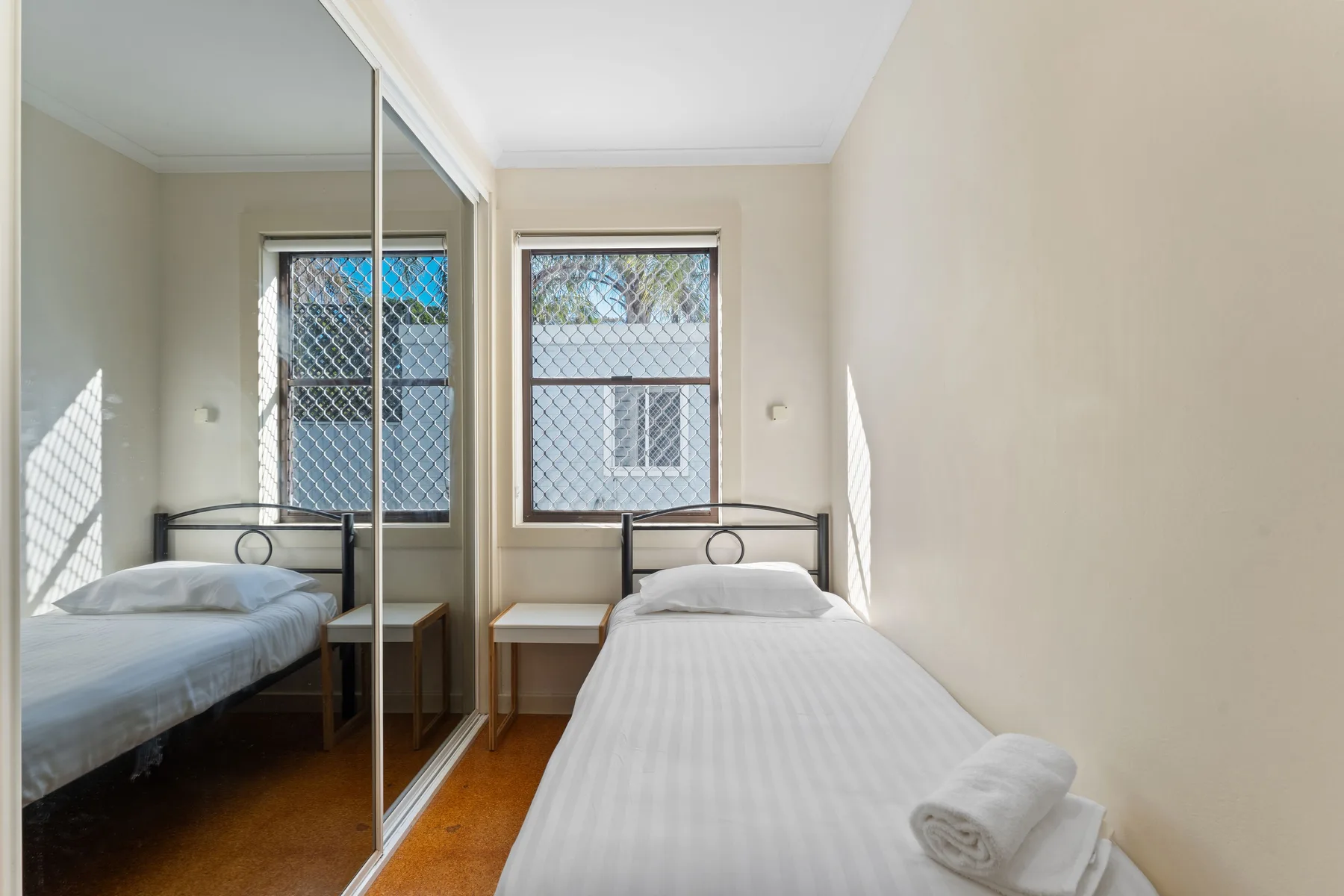 A bright bedroom with a bed beside two windows and mirrored wardrobe doors.