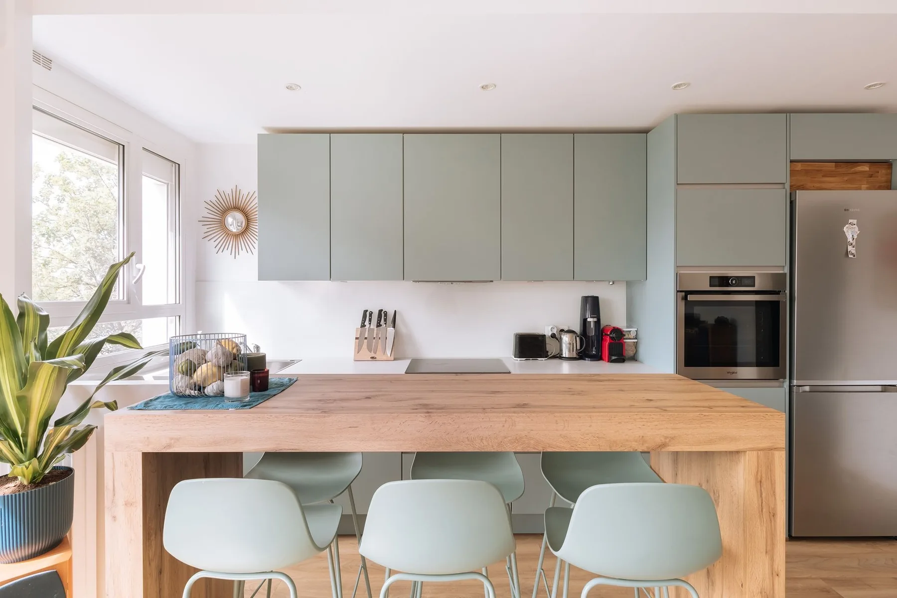 A bright kitchen with a wooden island and pale green seating.