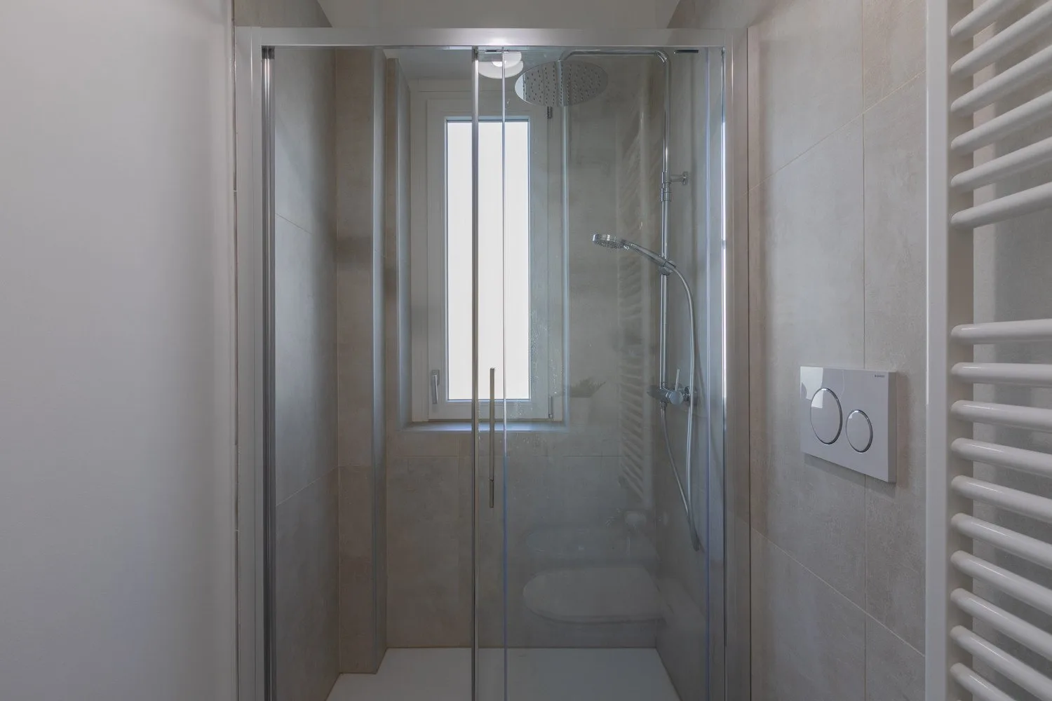 A tiled bathroom with a glass shower and a window.