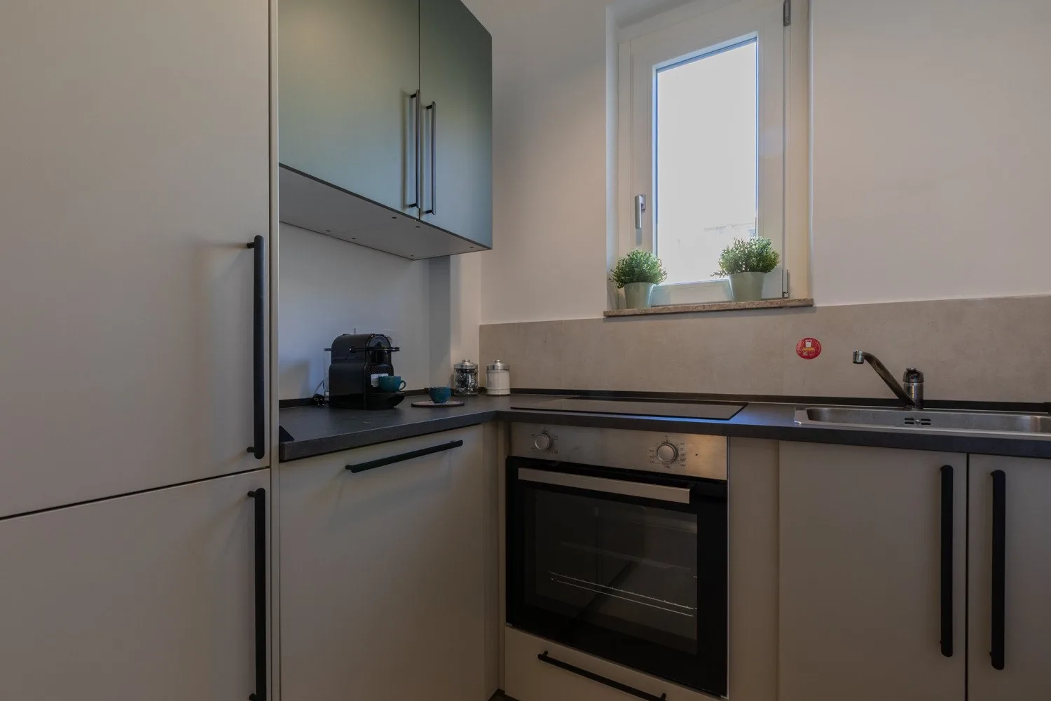 A compact kitchen with dark countertops, an oven, and a window above the sink.