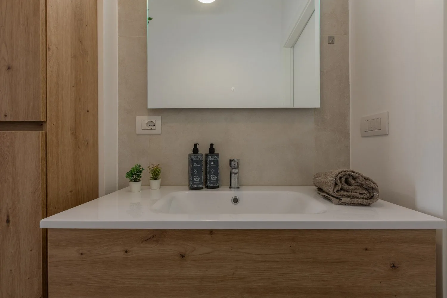 A bathroom vanity with a wide mirror, toiletries, and a folded towel.