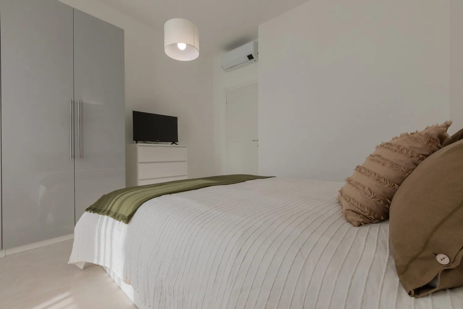 A bedroom with a neatly made bed and a television on a dresser.