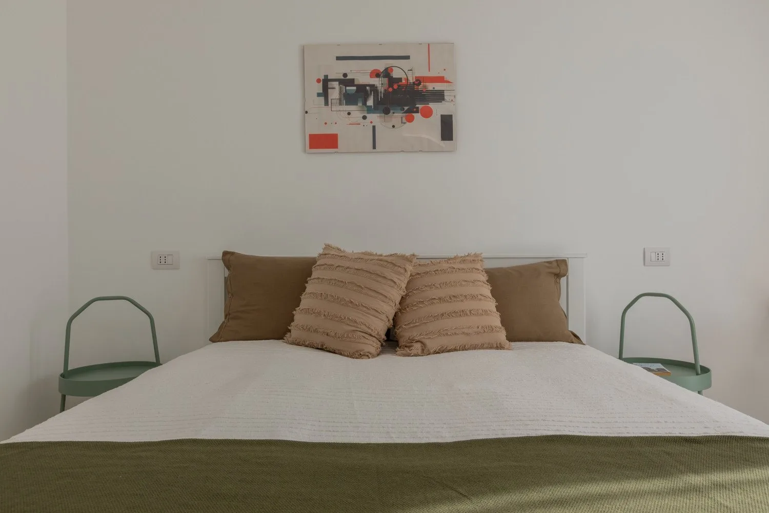 A bedroom with a neatly made bed and abstract artwork above the headboard.