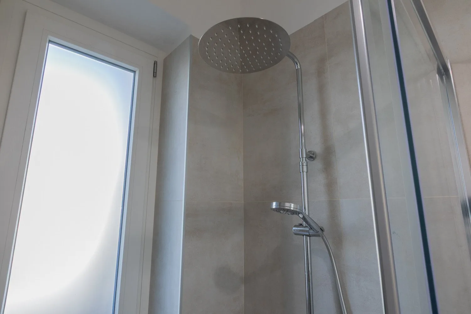 A tiled shower with a large overhead showerhead and handheld sprayer.