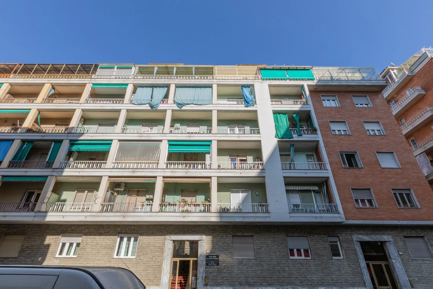 Apartment building facade with balconies and green awnings beneath a clear blue sky.