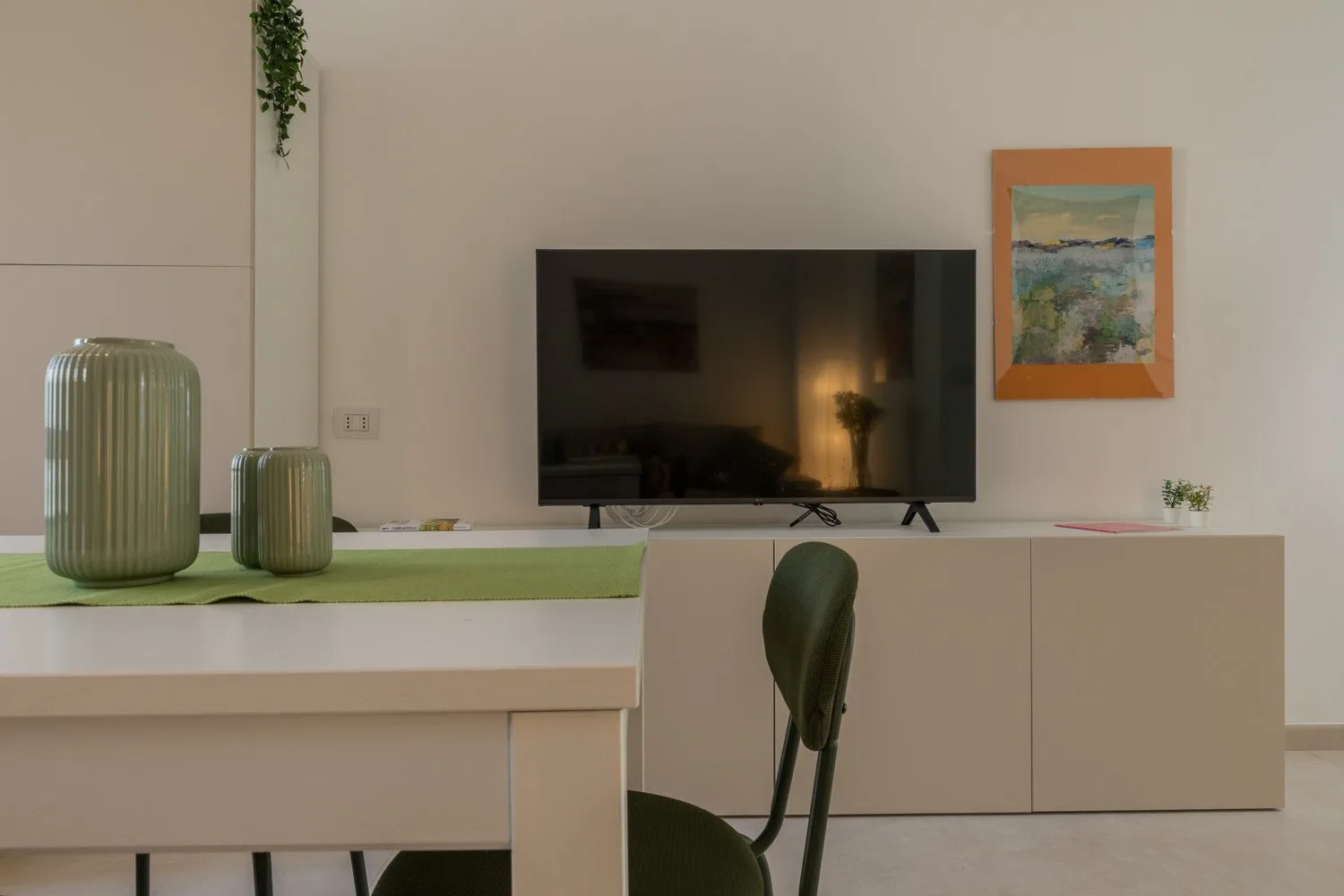 A living room with a television above a low cabinet and a dining table in the foreground.