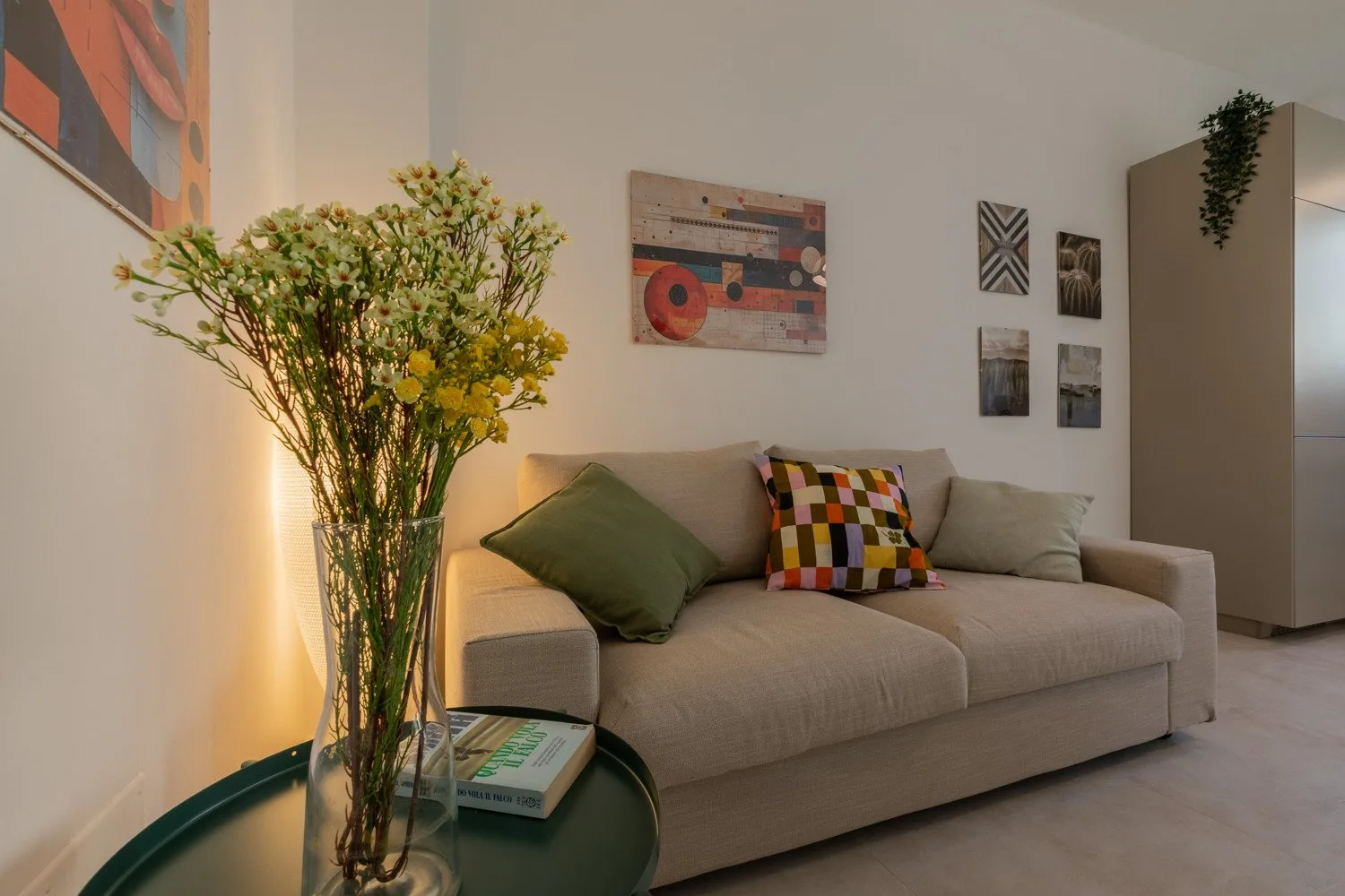 A living room with a beige sofa, colorful cushions, and framed wall art.