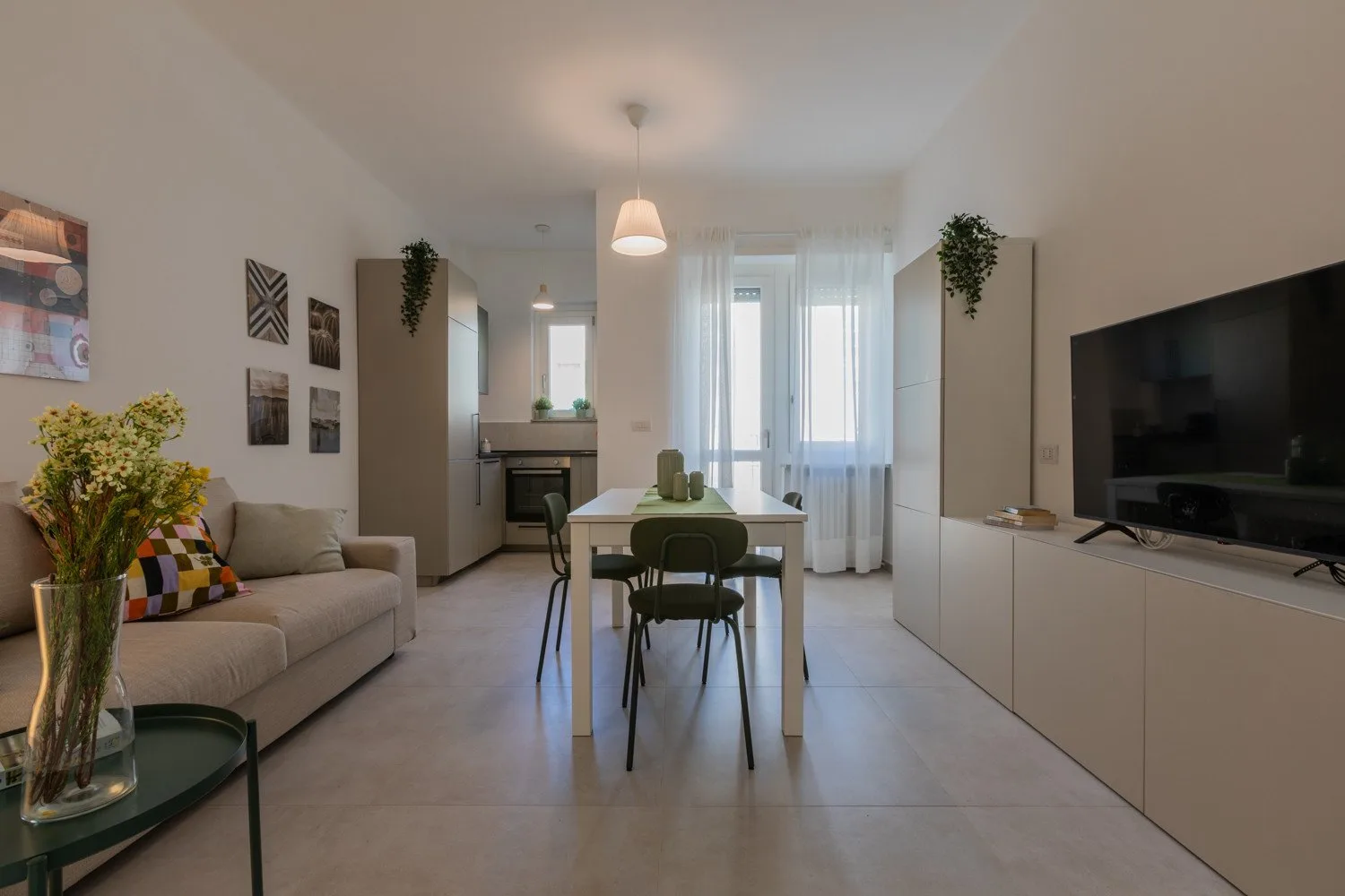 A bright living and dining area has a sofa, table, and large windows.
