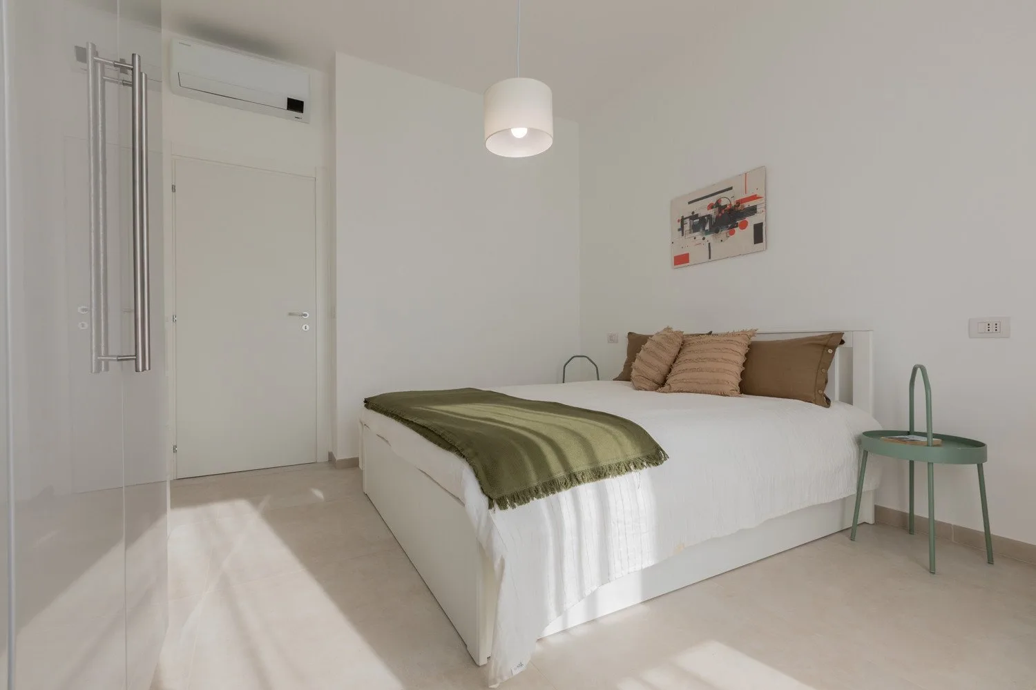 A bright bedroom with a white bed, green throw, and bedside table.
