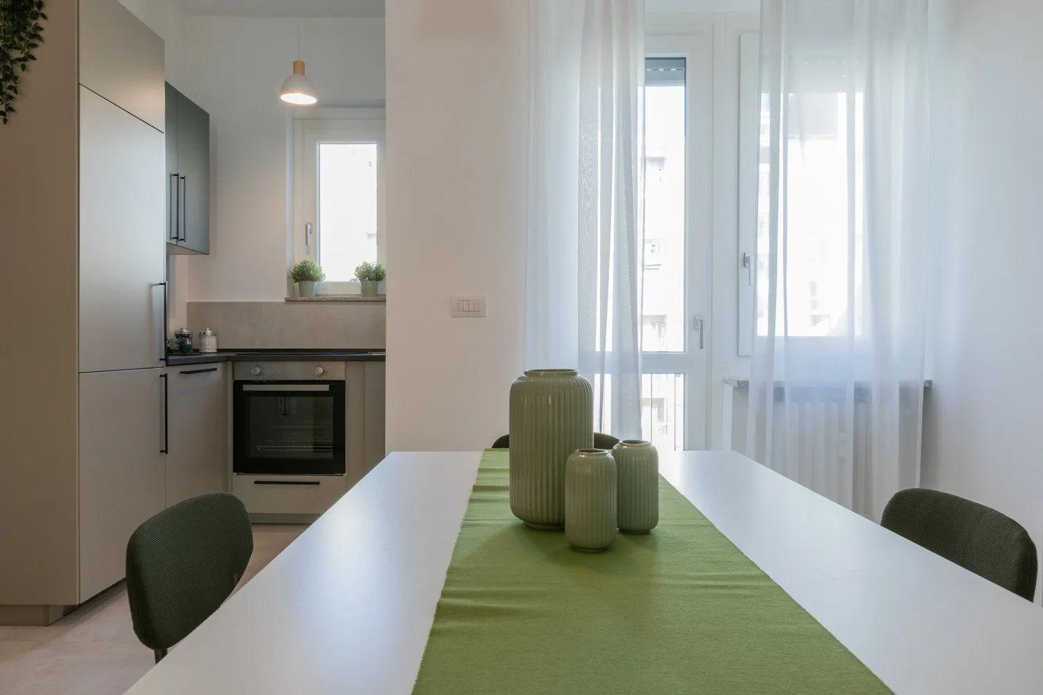 A dining table with a green runner sits beside a compact kitchen.