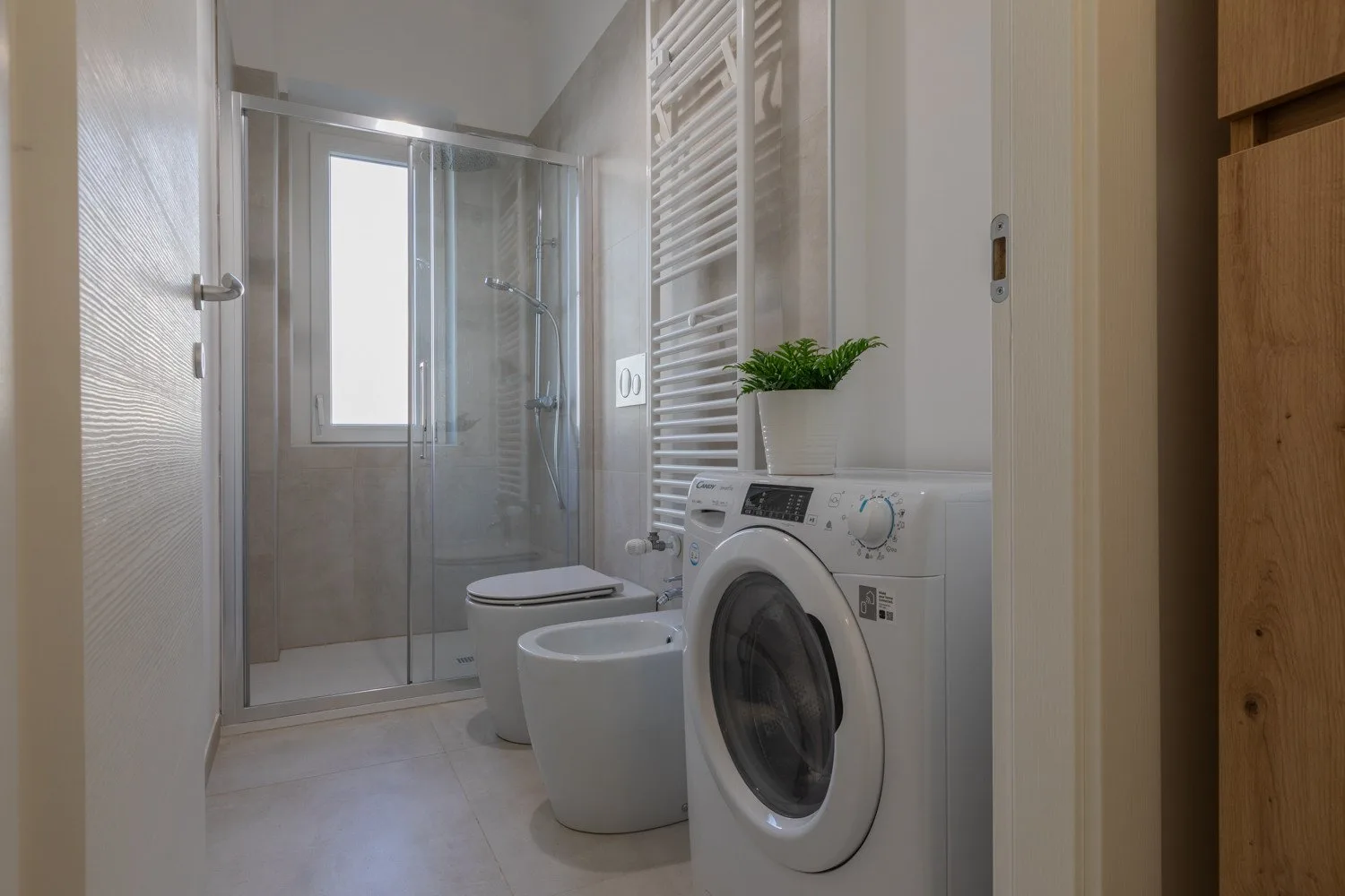 A bathroom with a glass shower, toilet, and washing machine.