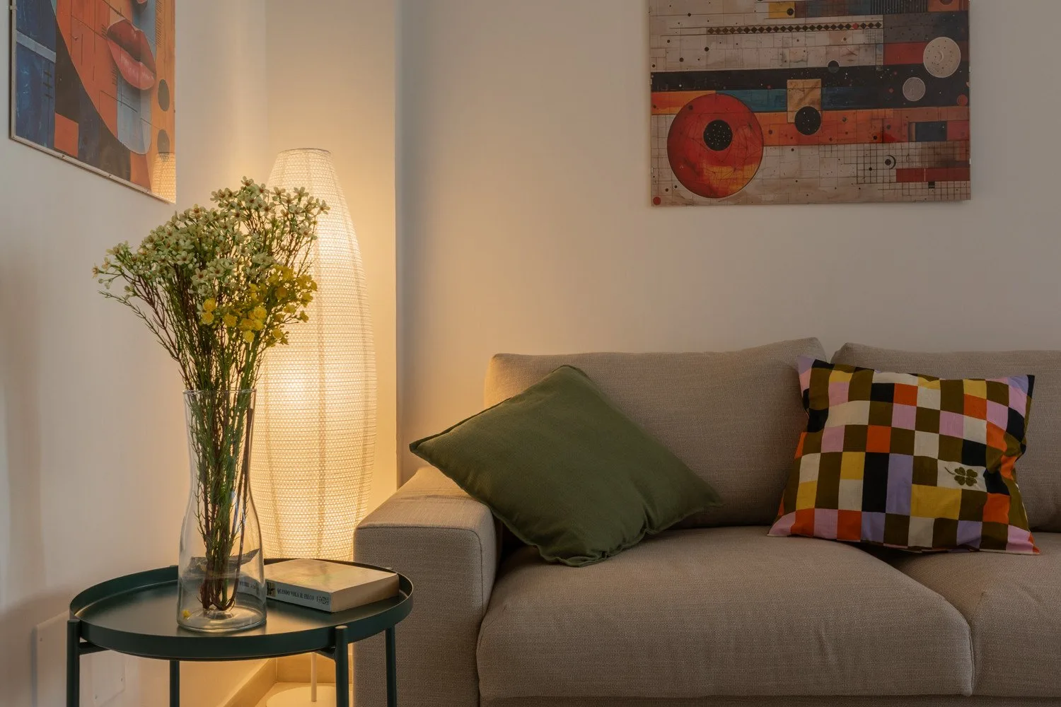 A living room seating area with a sofa, colorful cushions, and flowers beside a lamp.