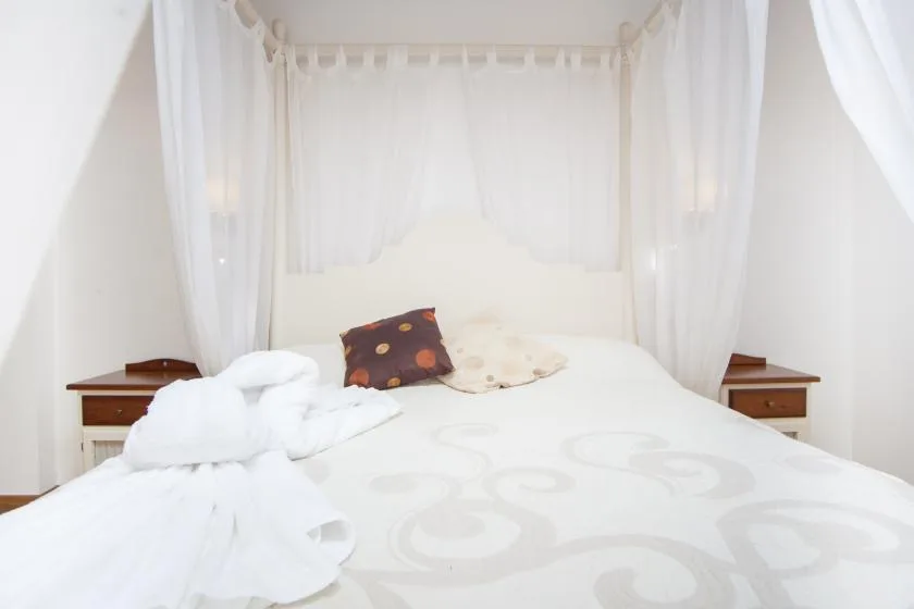 A bedroom with a white bed, sheer curtains, and small bedside tables.