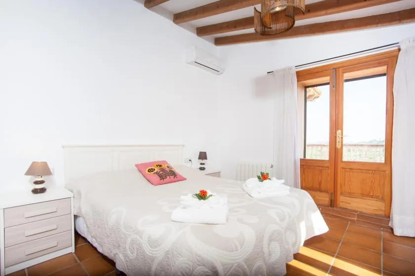 A bright bedroom with a double bed and wooden-framed glass doors.