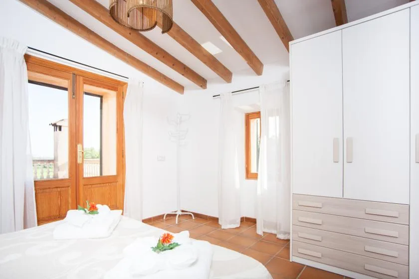 A bright bedroom with a bed, wooden doors, and exposed ceiling beams.
