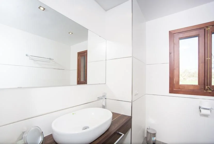 A bright bathroom with a white sink, large mirror, and wood-framed window.