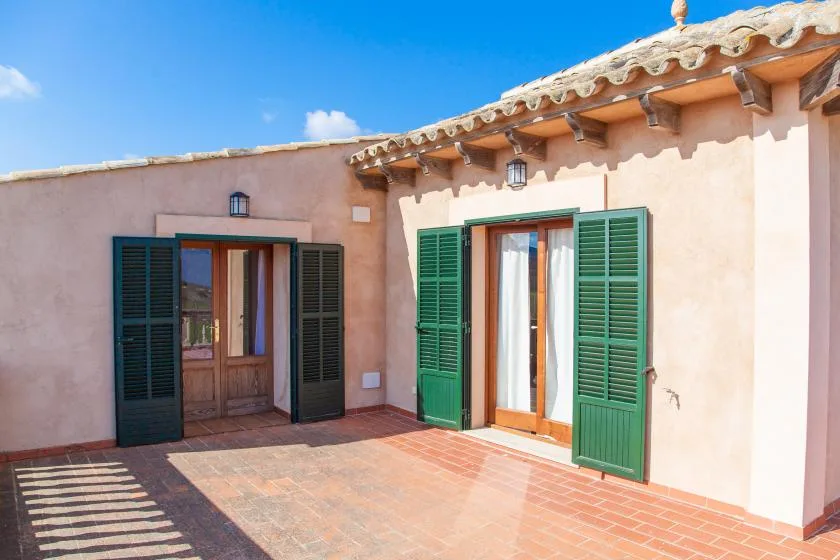 A sunlit patio with two doorways framed by open green shutters.