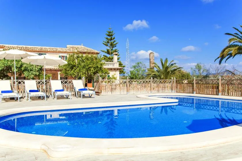 An outdoor swimming pool sits beside a tiled building and shaded seating.