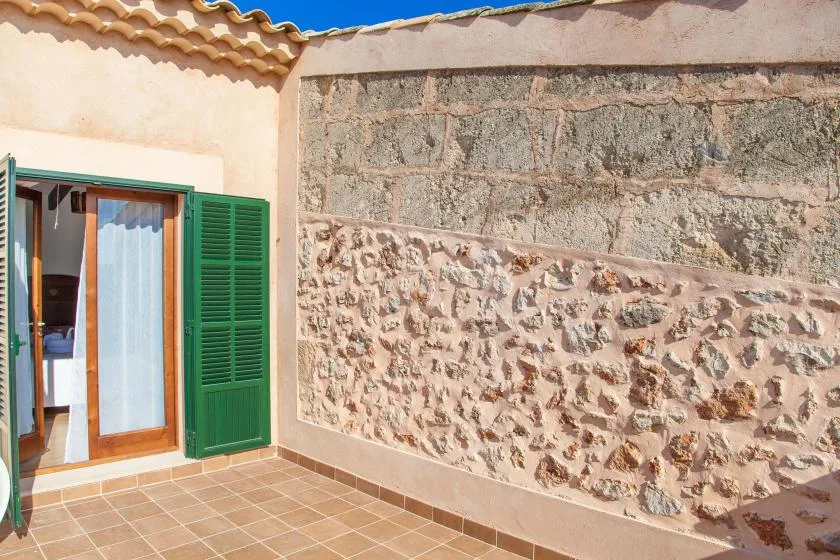 A tiled outdoor patio beside a stone wall, with a doorway and green shutters.