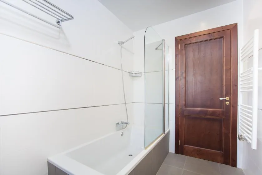 A bathroom with a bathtub, glass shower screen, and wooden door.