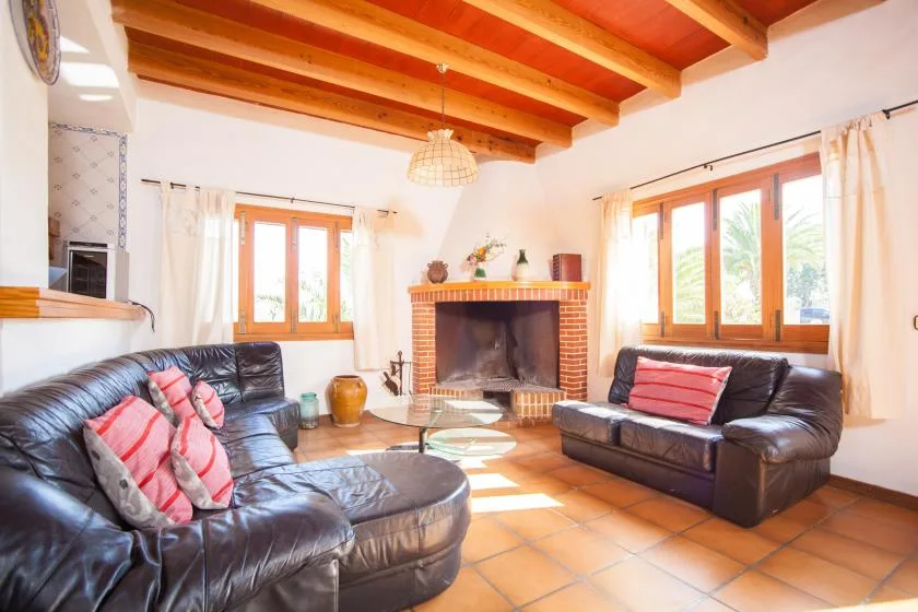 A living room with leather seating around a brick fireplace and wooden windows.